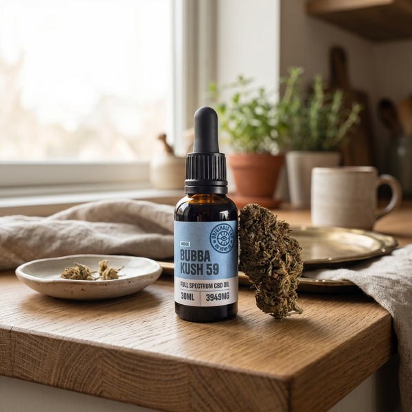 cbd oil next to cbd flower on a wooden kitchen table with plates and cups in the back ground.