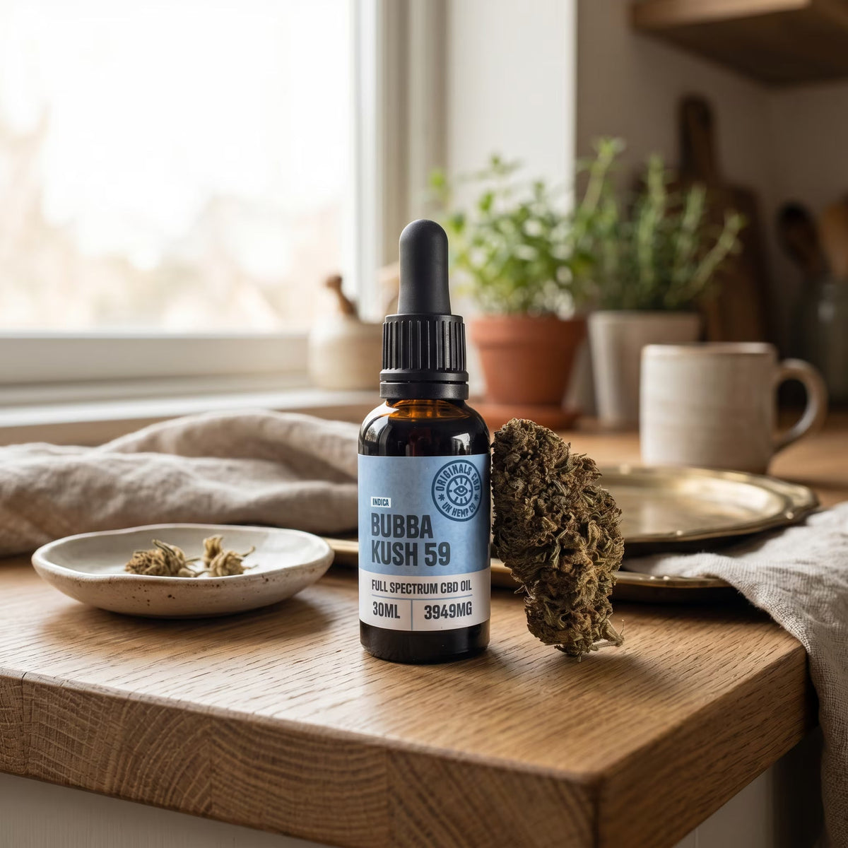 cbd oil next to cbd flower on a wooden kitchen table with plates and cups in the back ground.
