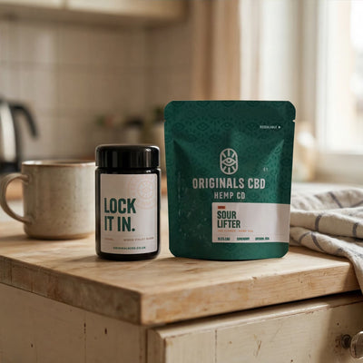 Mug, miron jar and originals cbd branded packaging on a wooden kitchen counter top, all neutral colours and background.