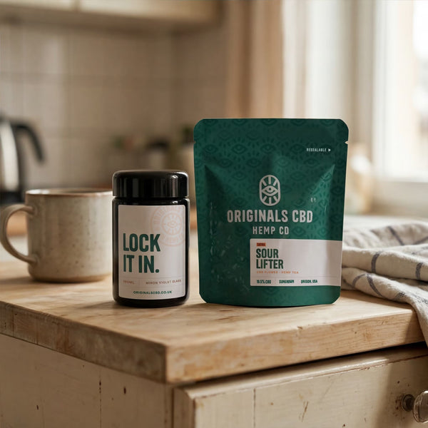 Mug, miron jar and originals cbd branded packaging on a wooden kitchen counter top, all neutral colours and background.