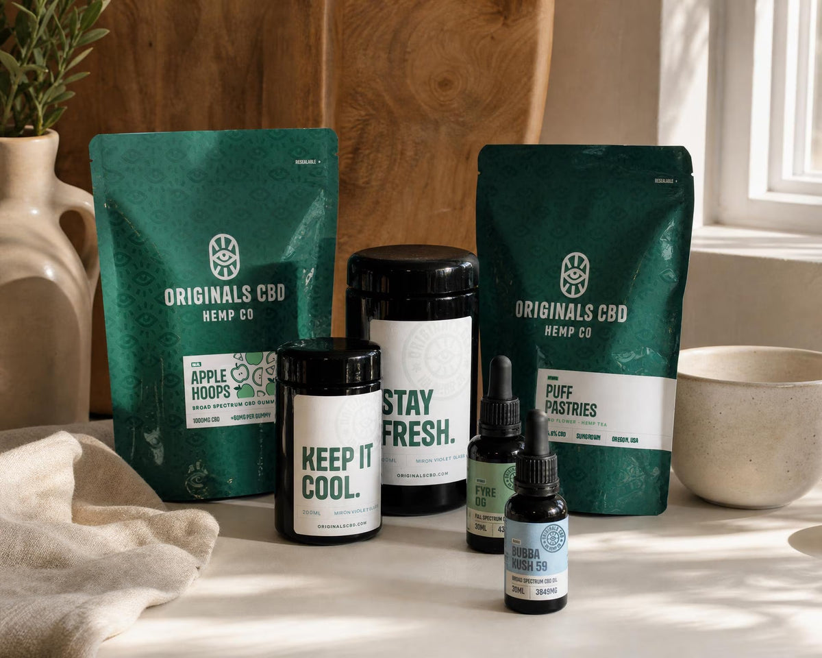 Originals CBD packaging line up, bags, jars and bottles on a white table, earthy tones.