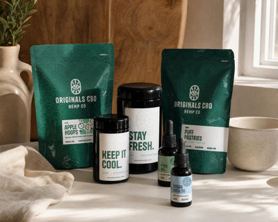 Originals CBD packaging line up, bags, jars and bottles on a white table, earthy tones.